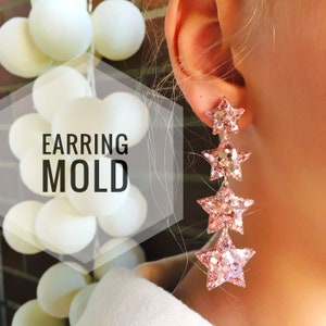 Könnte beinhalten: Ein Paar Hängeohrringe mit einem kaskadierenden Design aus fünf rosafarbenen Glitzersternen. Die Ohrringe sind aus einem glitzernden, funkelnden Material gefertigt.