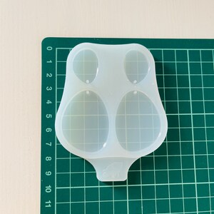 K&ouml;nnte beinhalten: Eine transparente Silikonform mit zwei ovalen Vertiefungen. Die Form ist zum Herstellen von Ohrringen oder anderen kleinen Schmuckst&uuml;cken gedacht.