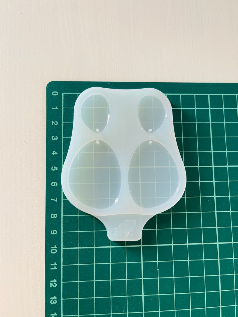 K&ouml;nnte beinhalten: Eine transparente Silikonform mit zwei ovalen Vertiefungen. Die Form ist zum Herstellen von Ohrringen oder anderen kleinen Schmuckst&uuml;cken gedacht.