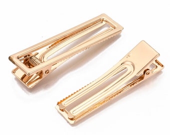 May include: Two gold metal hair clips. The clips are rectangular and have a spring mechanism to hold hair in place.