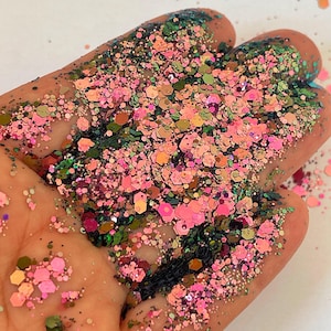 May include: A collection of loose craft glitter featuring a mix of hexagonal and fine particles in shades of bright pink, dark forest green, and metallic copper. The glitter pieces vary in size and reflect light, creating a textured appearance.