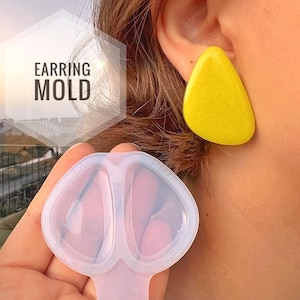 Könnte beinhalten: Eine durchscheinende Silikon-Ohrringform mit einer tropfenförmigen Vertiefung, begleitet von einem hellgelben, tropfenförmigen Ohrring. Der Text EARRING MOLD ist in einem weißen Sechseck auf der linken Seite des Bildes zu sehen.