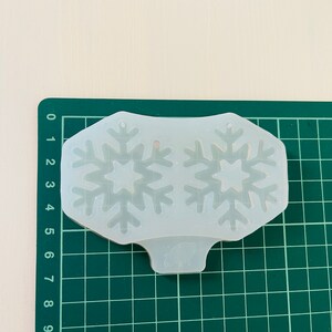 Op de afbeelding: Een transparante siliconen mal met twee sneeuwvlokontwerpen. De mal ligt op een groene snijmat.