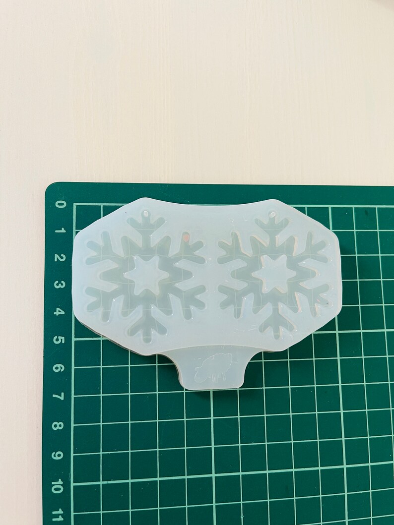 Op de afbeelding: Een transparante siliconen mal met twee sneeuwvlokontwerpen. De mal ligt op een groene snijmat.