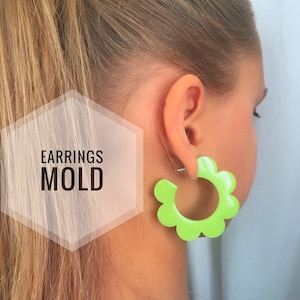 May include: Lime green flower-shaped hoop earrings. The earrings are made of plastic and have a smooth finish. The earrings are shown on a model with long blonde hair.