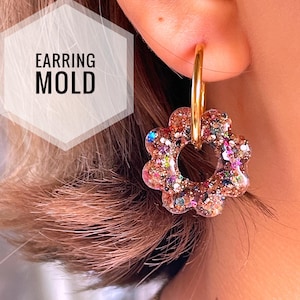 May include: Gold hoop earrings with a flower-shaped charm. The charm is made of clear resin with embedded glitter in shades of pink, gold, and brown.