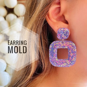 Peut inclure: Boucles d'oreilles carrées violettes avec une découpe carrée plus petite au centre. Les boucles d'oreilles sont recouvertes de paillettes irisées.