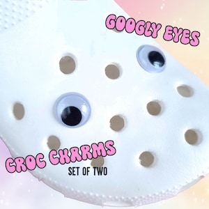 May include: Two white googly eyes with black pupils, labeled "Googly Eyes" and "Croc Charms Set of Two", on a white background.