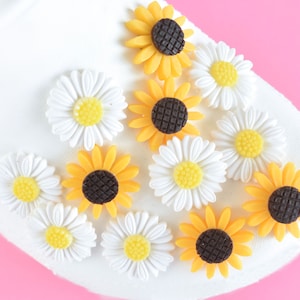 May include: A white surface with yellow and white flower embellishments. The flowers are arranged in a random pattern. The flowers are made of plastic and have a glossy finish.