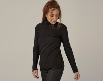 May include: A woman wearing a black turtleneck shirt and black pants. She is looking down at something off camera.