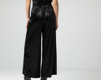May include: A black velvet jumpsuit with wide legs and a sleeveless top. The jumpsuit has a belt at the waist and is worn with black heeled boots.