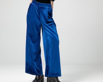 May include: A woman wearing a black velvet long-sleeved top and wide-legged blue velvet pants. She is wearing a black turban on her head.