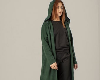 May include: A long, dark green hooded cardigan with a black top and black pants. The person is wearing black boots.