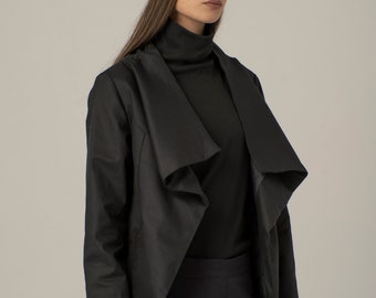 May include: A black, long-sleeved, draped jacket with a mock neck shirt and black pants. The person is wearing a black knit beanie.