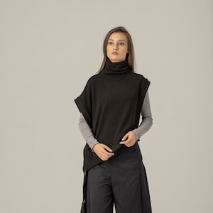 May include: A black turtleneck sweater with a draped, asymmetrical hemline. The sweater is worn with wide-leg, dark blue trousers and black boots.