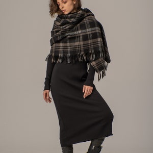 Puede incluir: Una mujer con un vestido midi de canal&eacute; negro y una bufanda de cuadros negros y marrones. Lleva botas negras de combate.