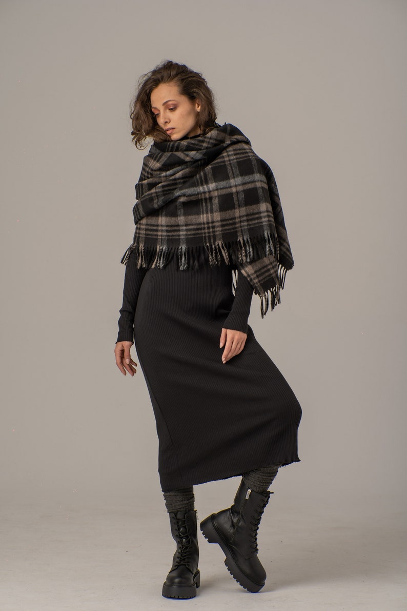 Puede incluir: Una mujer con un vestido midi de canal&eacute; negro y una bufanda de cuadros negros y marrones. Lleva botas negras de combate.