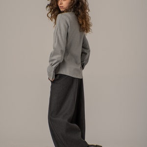May include: A woman wearing a gray collared shirt and dark gray wide-leg pants. She is wearing black lace-up boots.
