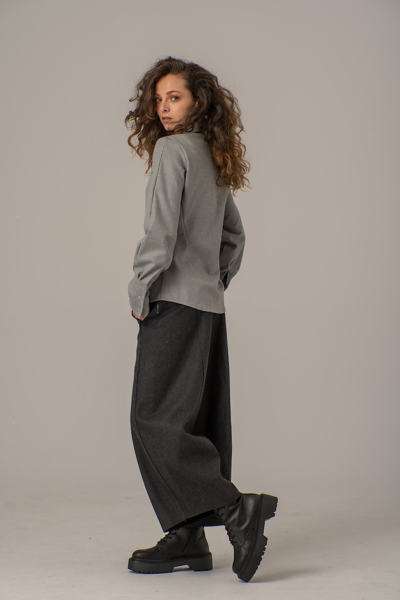 May include: A woman wearing a gray collared shirt and dark gray wide-leg pants. She is wearing black lace-up boots.