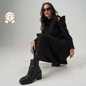 May include: A black dress with a cut-out shoulder detail and long sleeves. The dress is paired with black ankle boots.