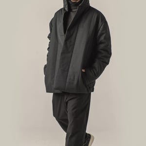 May include: A black quilted jacket with a high collar and a zipper closure. The jacket has a relaxed fit and is worn over a black turtleneck.