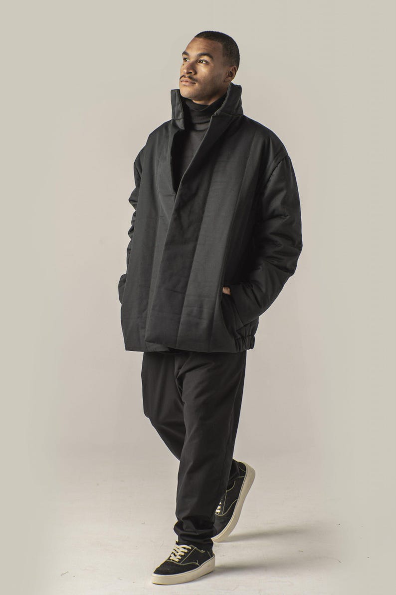 May include: A black quilted jacket with a high collar and a zipper closure. The jacket has a relaxed fit and is worn over a black turtleneck.