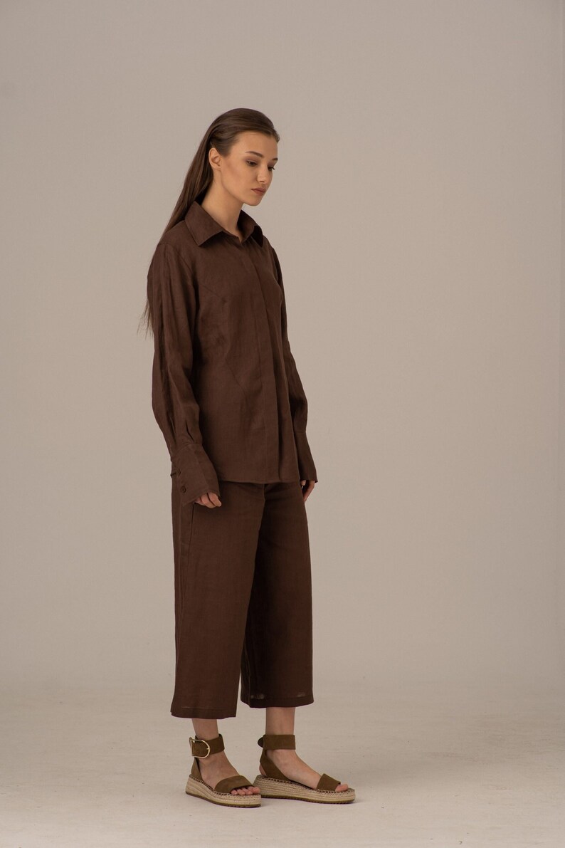 May include: A brown linen shirt and matching wide-leg trousers. The shirt has a collared neckline and long sleeves. The trousers have a straight leg and a cropped length.