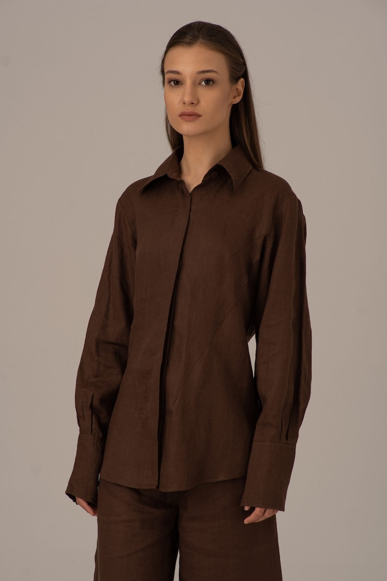 May include: A brown linen shirt and trousers set with a collared shirt and long sleeves. The shirt has a button-up front and a slightly fitted silhouette.