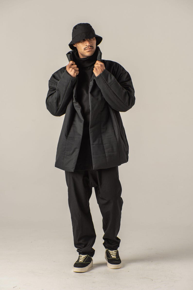 May include: A black quilted jacket with a high collar and a black bucket hat. The person is wearing black pants and black sneakers.