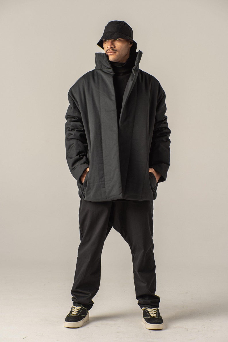 May include: A black puffer jacket with a high collar and a black turtleneck underneath. The person is wearing black pants and black sneakers.