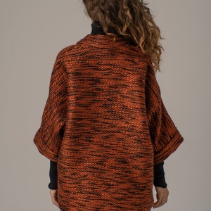 Op de afbeelding: Een roestkleurige gebreide cardigan met een zwart en roest marmerpatroon. De cardigan heeft een ontspannen pasvorm en een licht getailleerde lengte.