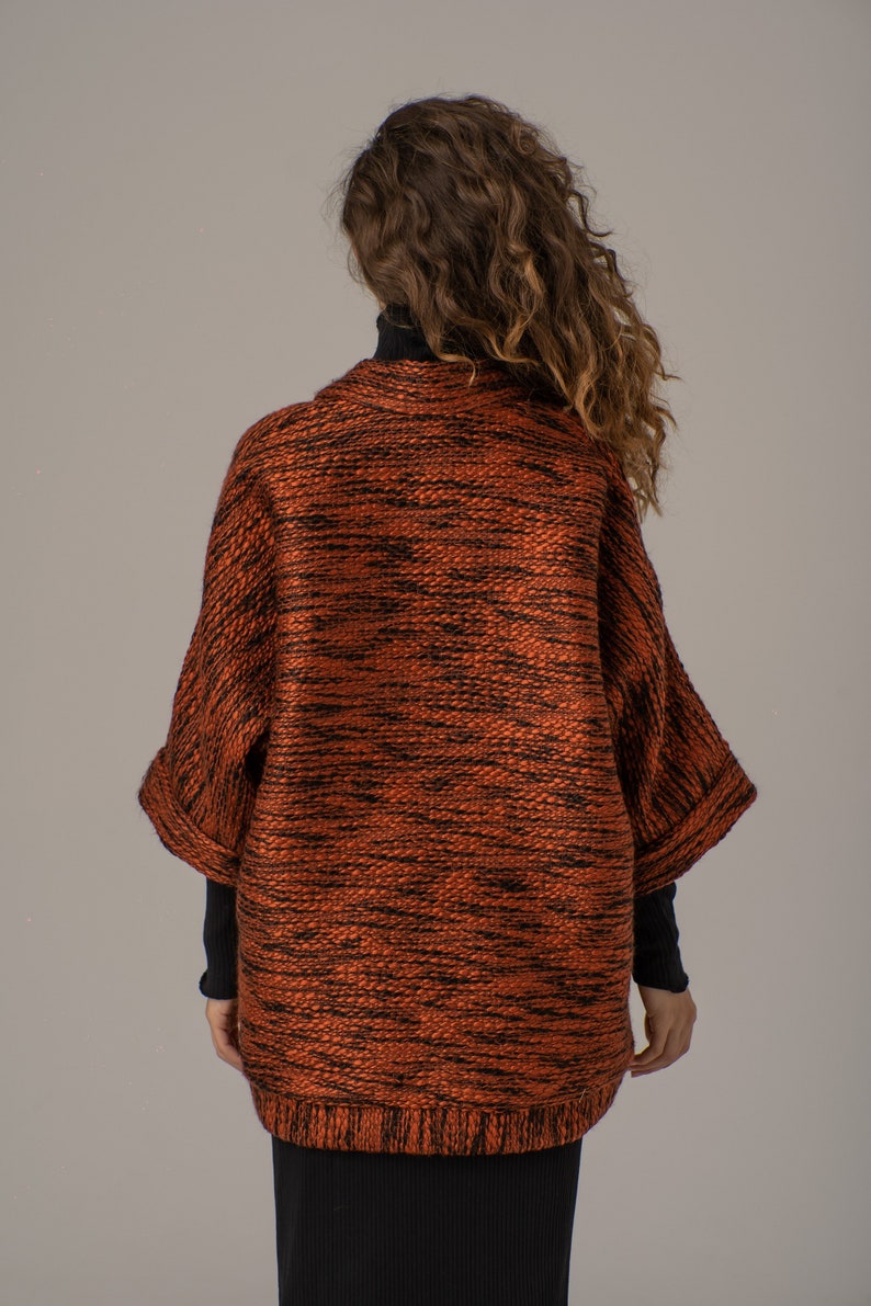 Op de afbeelding: Een roestkleurige gebreide cardigan met een zwart en roest marmerpatroon. De cardigan heeft een ontspannen pasvorm en een licht getailleerde lengte.