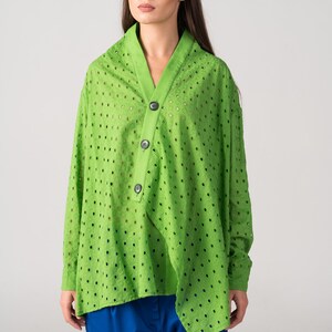 May include: A lime green, long-sleeved, button-up shirt with a  pattern of small, evenly spaced holes. The shirt has a V-neck and a slightly asymmetrical hemline.