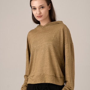 K&ouml;nnte beinhalten: Ein beigefarbener Kapuzenpullover mit langen &Auml;rmeln und einem Kordelzug am Saum. Der Kapuzenpullover wird mit einer schwarzen Hose kombiniert. Das Model tr&auml;gt den Kapuzenpullover und die Hose. Der Kapuzenpullover ist aus einem weichen, leichten Material.