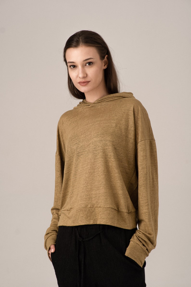 K&ouml;nnte beinhalten: Ein beigefarbener Kapuzenpullover mit langen &Auml;rmeln und einem Kordelzug am Saum. Der Kapuzenpullover wird mit einer schwarzen Hose kombiniert. Das Model tr&auml;gt den Kapuzenpullover und die Hose. Der Kapuzenpullover ist aus einem weichen, leichten Material.