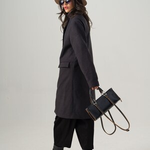 May include: A dark gray coat with a tailored fit, paired with black culottes and chunky black boots. A tan fedora and sunglasses complete the look. A black rectangular handbag with brown straps is held in the hand.