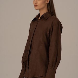 May include: A brown linen shirt with long sleeves and a button-up front. The shirt has a relaxed fit and a slightly oversized silhouette.