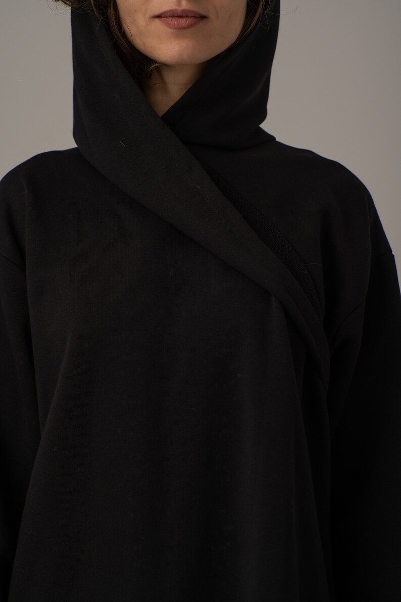Pode incluir: Uma camisola de capuz preta com um capuz longo e drapeado. O capuz est&aacute; dobrado sobre si mesmo e o tecido &eacute; suave e liso.