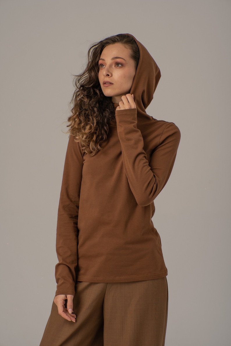 May include: A brown long-sleeved shirt with a hood. The shirt has a turtleneck collar and is made of a soft, comfortable fabric.