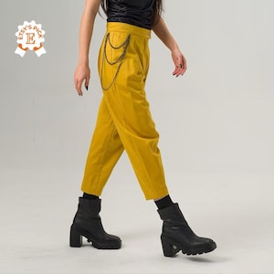 May include: Mustard yellow high-waisted pants with a chain detail at the side. The pants are cropped and have a relaxed fit.
