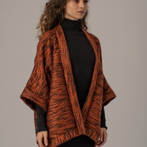 Op de afbeelding: Een langarmige, oranje en zwarte gebreide cardigan met een shawlkraag. De cardigan is open aan de voorkant en heeft een losse pasvorm.