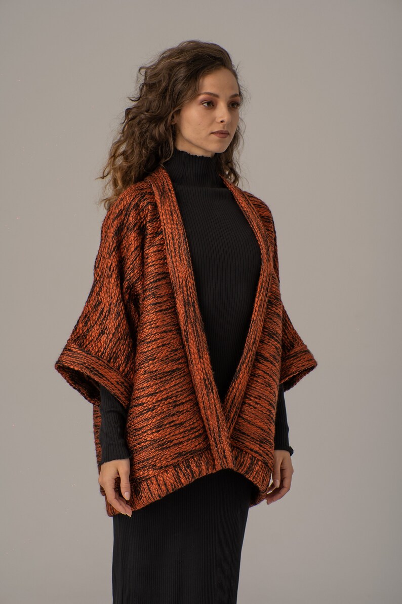 Op de afbeelding: Een langarmige, oranje en zwarte gebreide cardigan met een shawlkraag. De cardigan is open aan de voorkant en heeft een losse pasvorm.