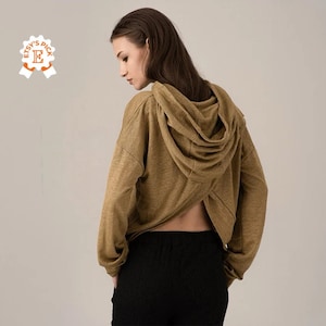 K&ouml;nnte beinhalten: Ein beigefarbener Kapuzenpullover mit einem einzigartigen R&uuml;ckendesign, kombiniert mit schwarzer Hose. Der Kapuzenpullover hat eine drapierte Kapuze und lange &Auml;rmel. Das Model ist von hinten zu sehen. Das Etsy's Pick-Abzeichen ist sichtbar.