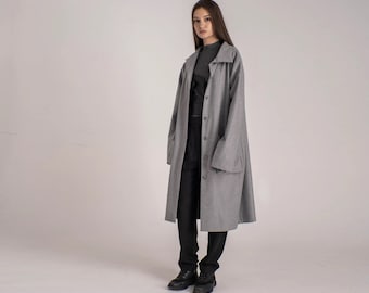 May include: A gray long-sleeved coat with a button closure and large pockets. The coat is worn over a black top and black pants.