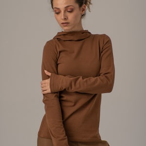 May include: A brown long-sleeved shirt with a high neck and a relaxed fit. The shirt is made of a soft, comfortable fabric.