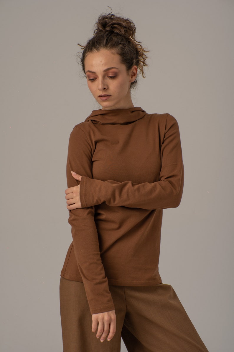 May include: A brown long-sleeved shirt with a high neck and a relaxed fit. The shirt is made of a soft, comfortable fabric.