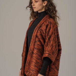 Op de afbeelding: Een langarmige, oranje en zwarte gebreide cardigan met een ontspannen pasvorm. De cardigan heeft een shawlkraag en een knoopsluiting.