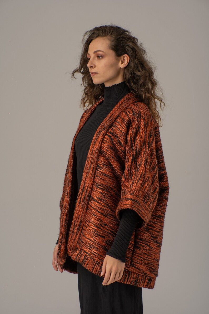 Op de afbeelding: Een langarmige, oranje en zwarte gebreide cardigan met een ontspannen pasvorm. De cardigan heeft een shawlkraag en een knoopsluiting.