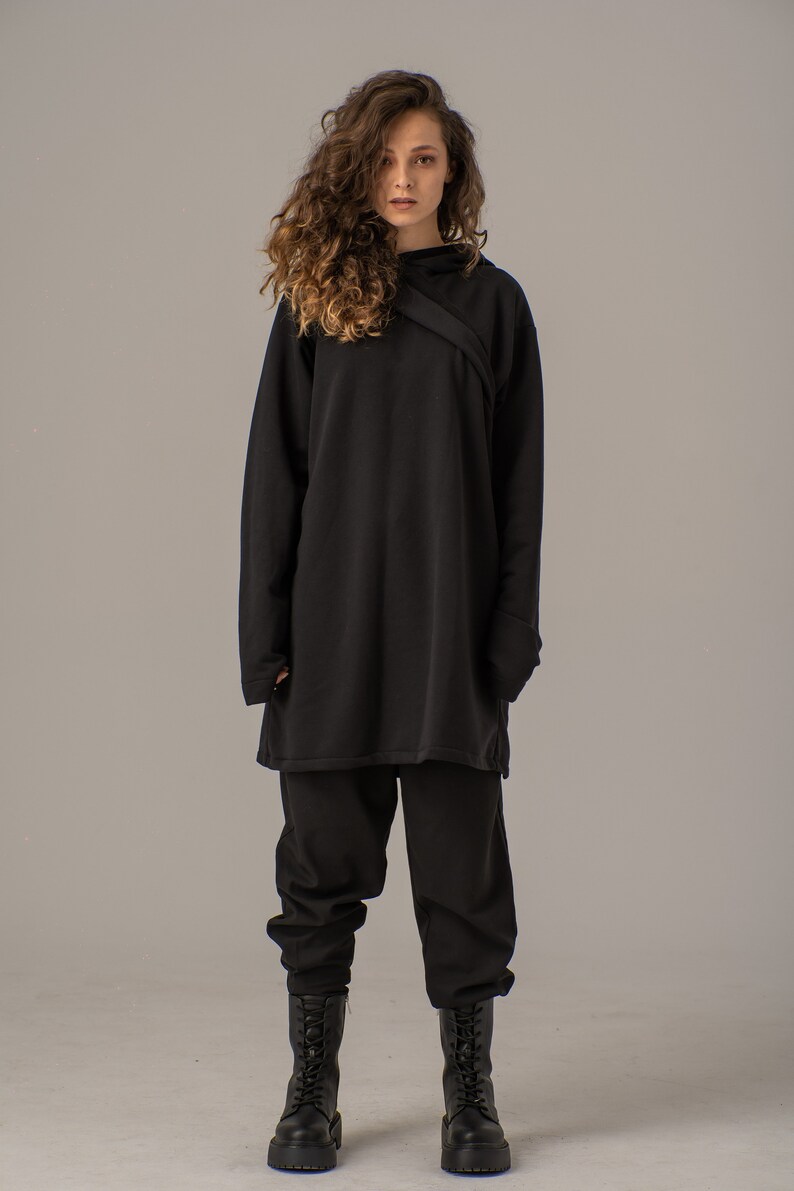 Pode incluir: Uma blusa preta de manga comprida com um detalhe cruzado na gola. A blusa &eacute; combinada com cal&ccedil;as pretas e botas pretas de cadar&ccedil;o.