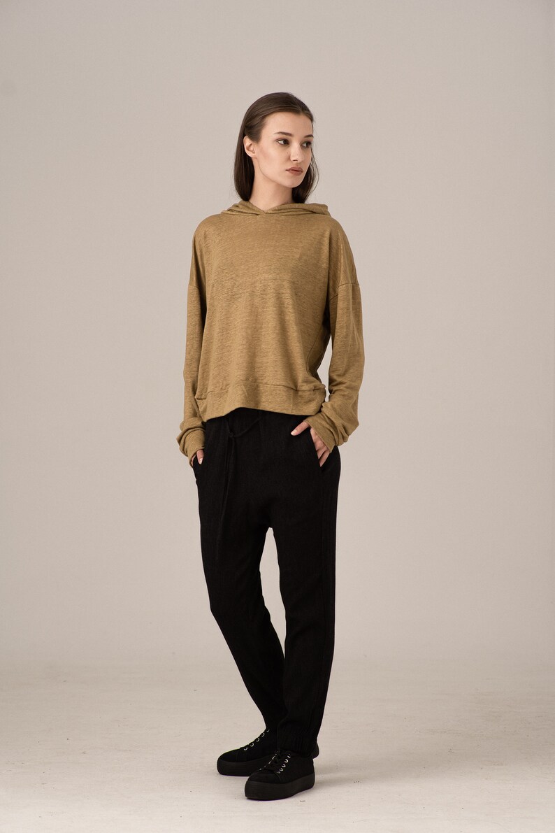 K&ouml;nnte beinhalten: Ein l&auml;ssiges Outfit mit einem beigefarbenen Kapuzenpullover und einer schwarzen Hose. Der lang&auml;rmlige Kapuzenpullover hat eine Kapuze mit Kordelzug und wird mit einer locker sitzenden schwarzen Hose kombiniert. Schwarze Schuhe vervollst&auml;ndigen das Ensemble.